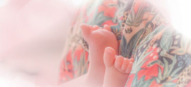 Stopki niemowlaka oparte o kwiecistą suknię cioci